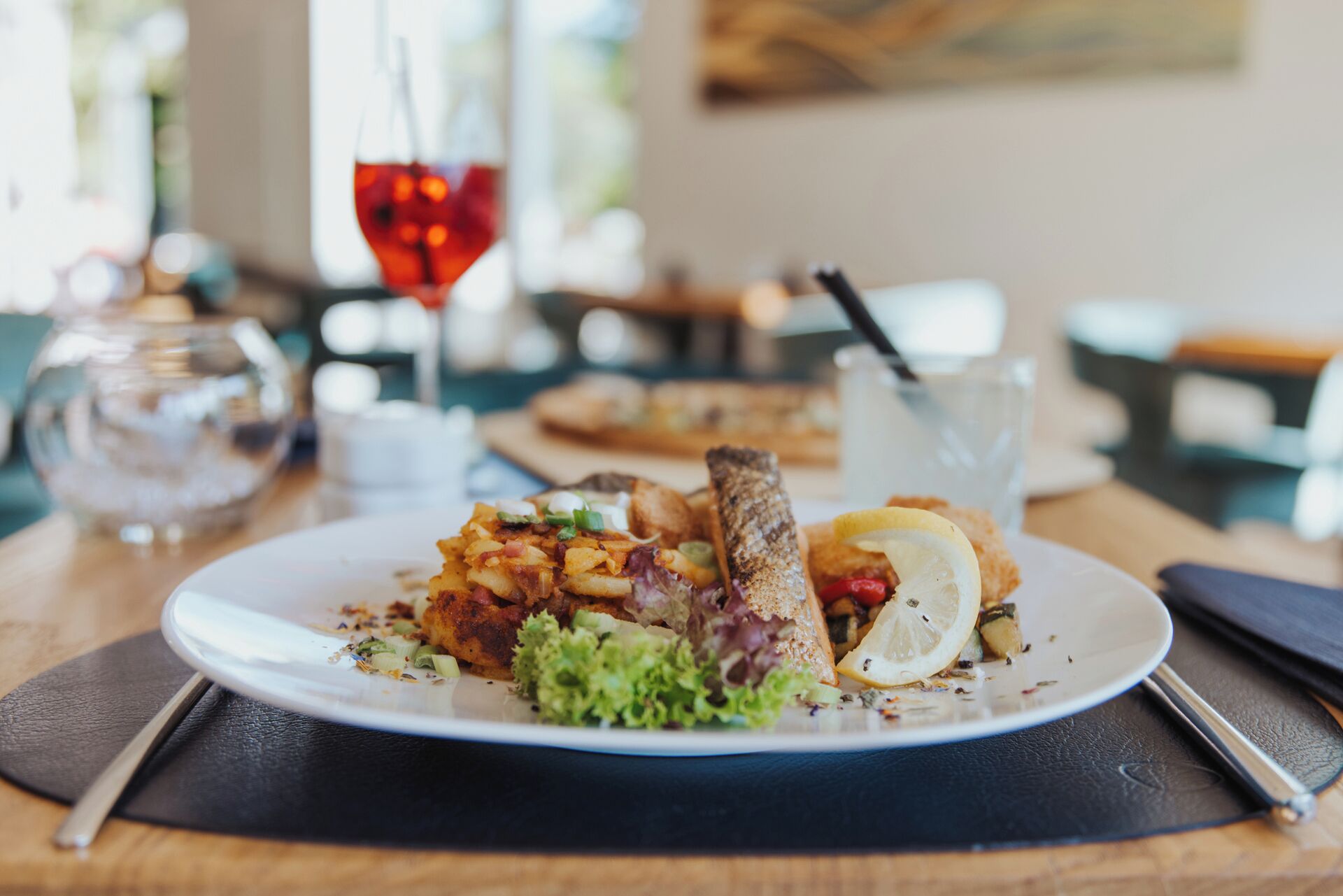 A plate of food with a fish fillet, potatoes, and a lemon wedge on a white plate.