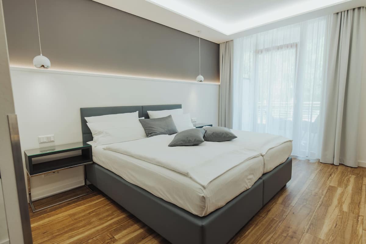 A modern bedroom with a large bed, bedside tables, and a view of the outdoors through sheer curtains.