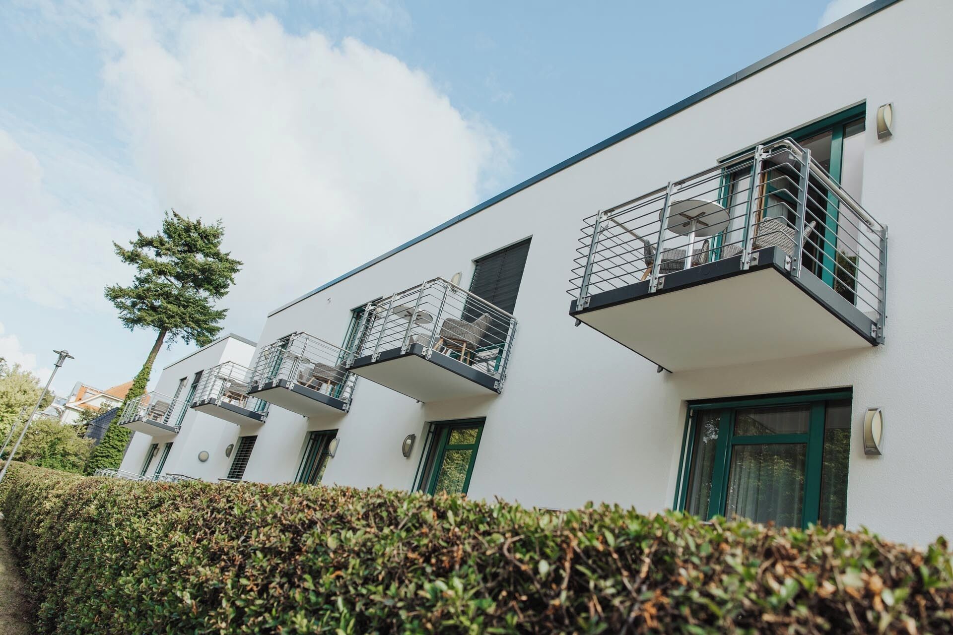 A modern building with multiple balconies, each with a metal railing and a small table.