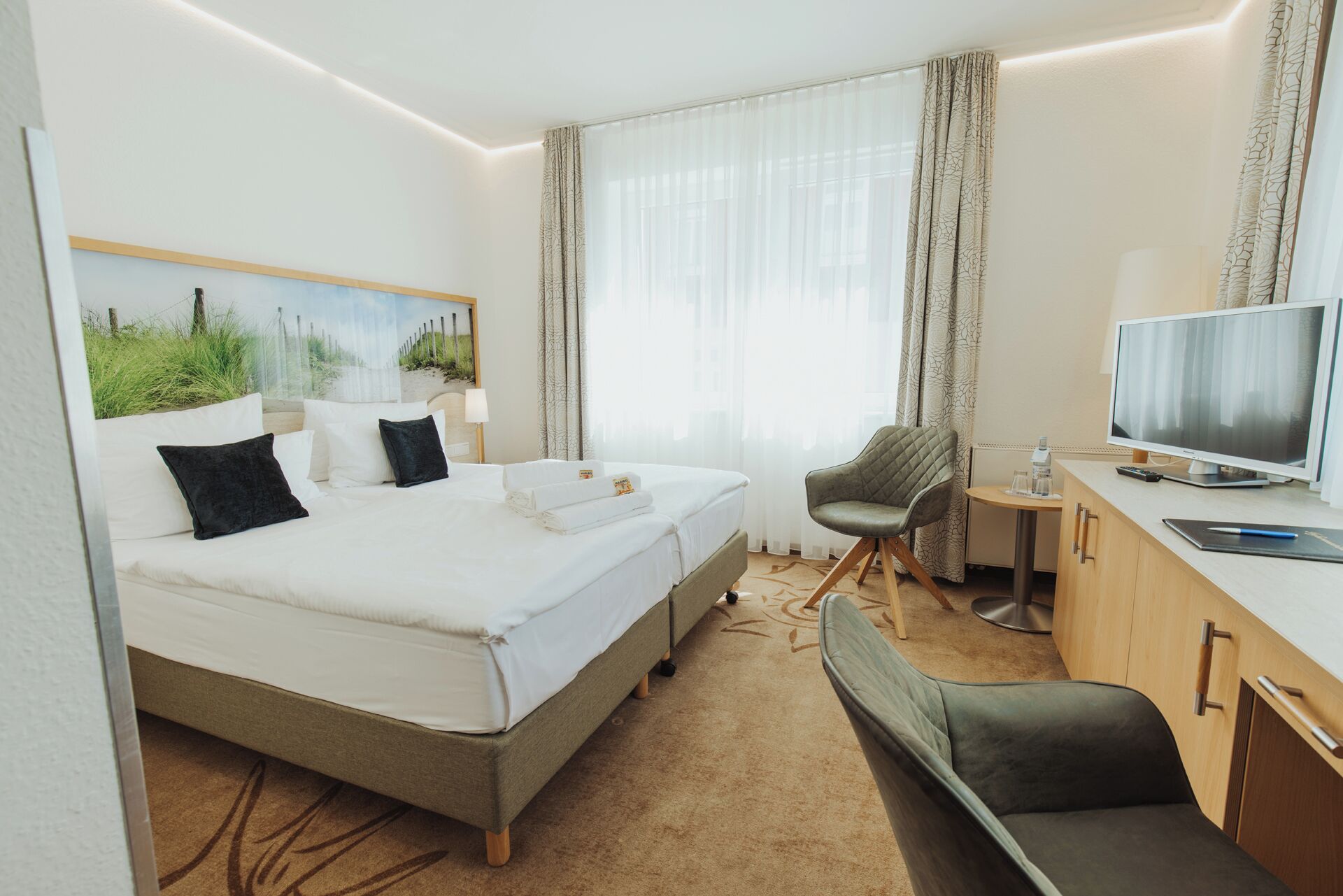A hotel room with a bed, a desk with a computer, a chair, and a television.