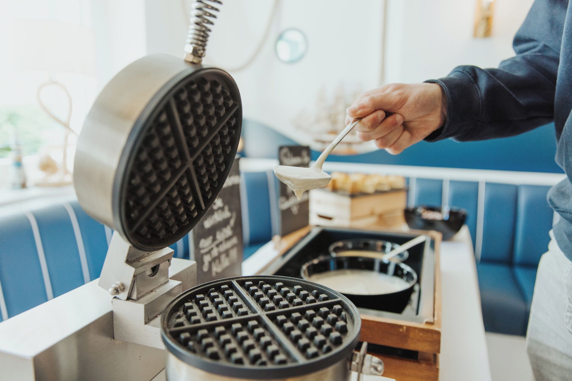 A waffle iron with a person using a spoon to handle the waffle.
