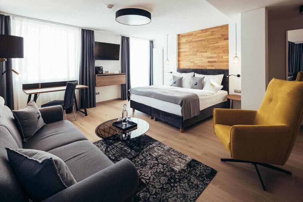 A modern hotel room with a bed, sofa, desk, and a yellow armchair.