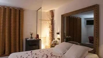 Una habitación de hotel con una cama grande, un espejo, una mesita de noche y una pared de ladrillo.