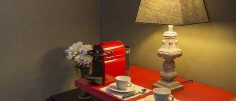 A small table with a red lamp, a coffee maker, and two cups on a red table.