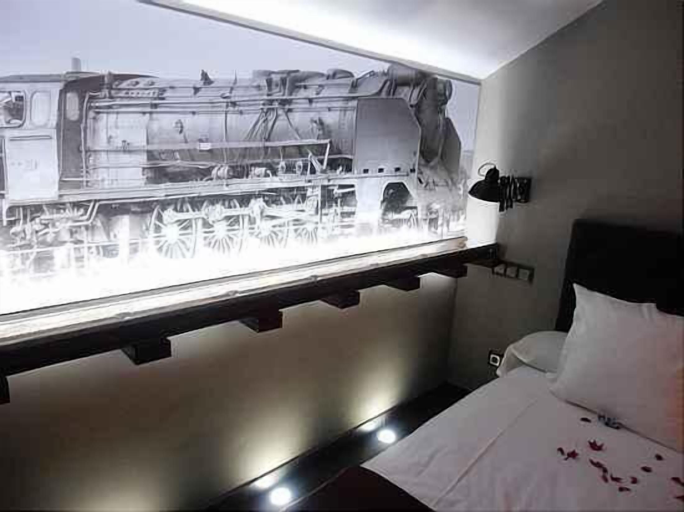 A hotel room with a bed, a nightstand, and a wall-mounted light fixture.
