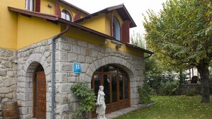 Un edificio de piedra con fachada amarilla, una puerta de madera y una estatua en el jardín.