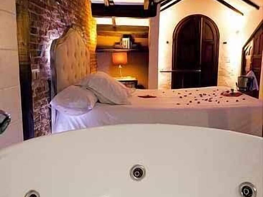 A room with a large bathtub, a bed, and a brick wall.