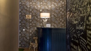 Zona de recepción con papel tapiz floral, un escritorio con lámpara y una pared con notas escritas a mano.