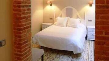A bedroom with a brick archway, a bed, two bedside tables, and wall-mounted lamps.