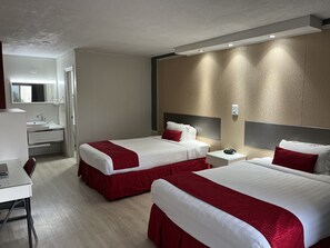 Et hotelværelse med to senge, et skrivebord, en stol og et badeværelse med håndvask og spejl.