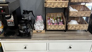 A kitchen counter with a coffee machine, a water dispenser, and wicker baskets containing condiments and utensils.