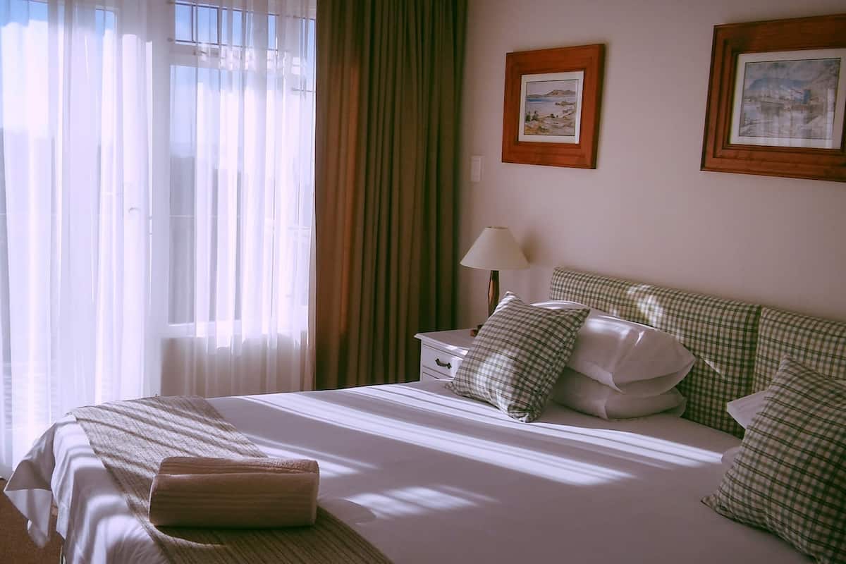 A hotel room with a large bed, a nightstand, a lamp, and two framed pictures on the wall.