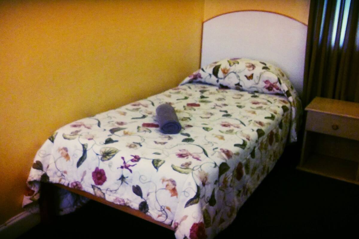 A small bed with a floral bedspread and a single rolled-up towel.