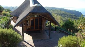 A thatched-roof cottage with a stone foundation, a wooden porch, and a view of the surrounding landscape. - Carmel Guest Farm (Wilderness)