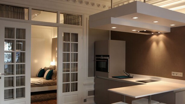 Una cocina moderna con horno integrado, encimera blanca y zona de estar con bancos.