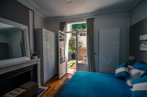 Un dormitorio con una cama grande, una chimenea y vistas a un jardín a través de una puerta abierta.