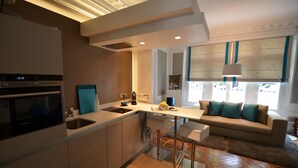 Una cocina moderna con horno integrado, un lavamanos y una zona de bar. Hay un sofá y una mesa de centro en la sala de estar.
