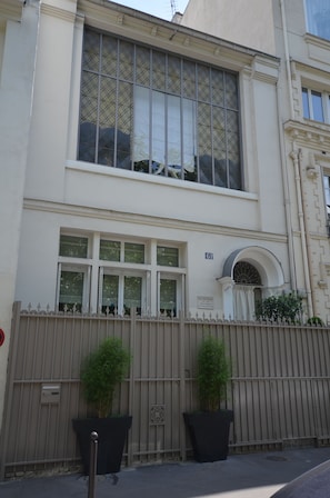 A building with a large window, a gated entrance, and two potted plants. - Le 61 Berthier (Paris)