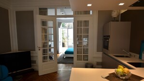 Una cocina moderna con horno empotrado, refrigerador y un comedor con una mesa y un bol de fruta.