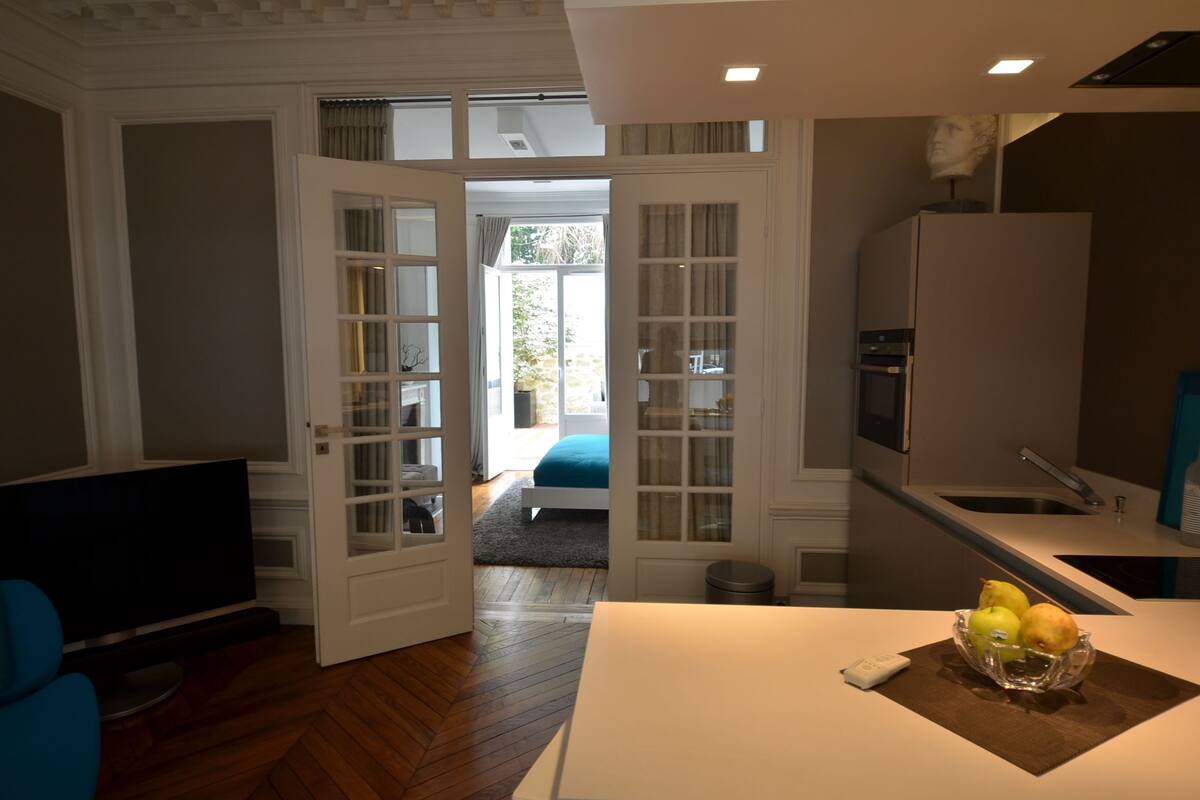 A modern kitchen with a built-in oven, a refrigerator, and a dining area with a table and a bowl of fruit.