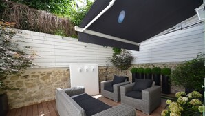 Un patio con mobiliario de mimbre, pared de piedra y toldo negro.