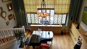 Un comedor con una mesa negra, una araña y una ventana con cortinas estampadas.