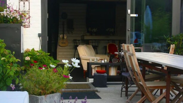 An outdoor patio with a dining table, chairs, and a guitar in the background. - Kathome (Bondues)