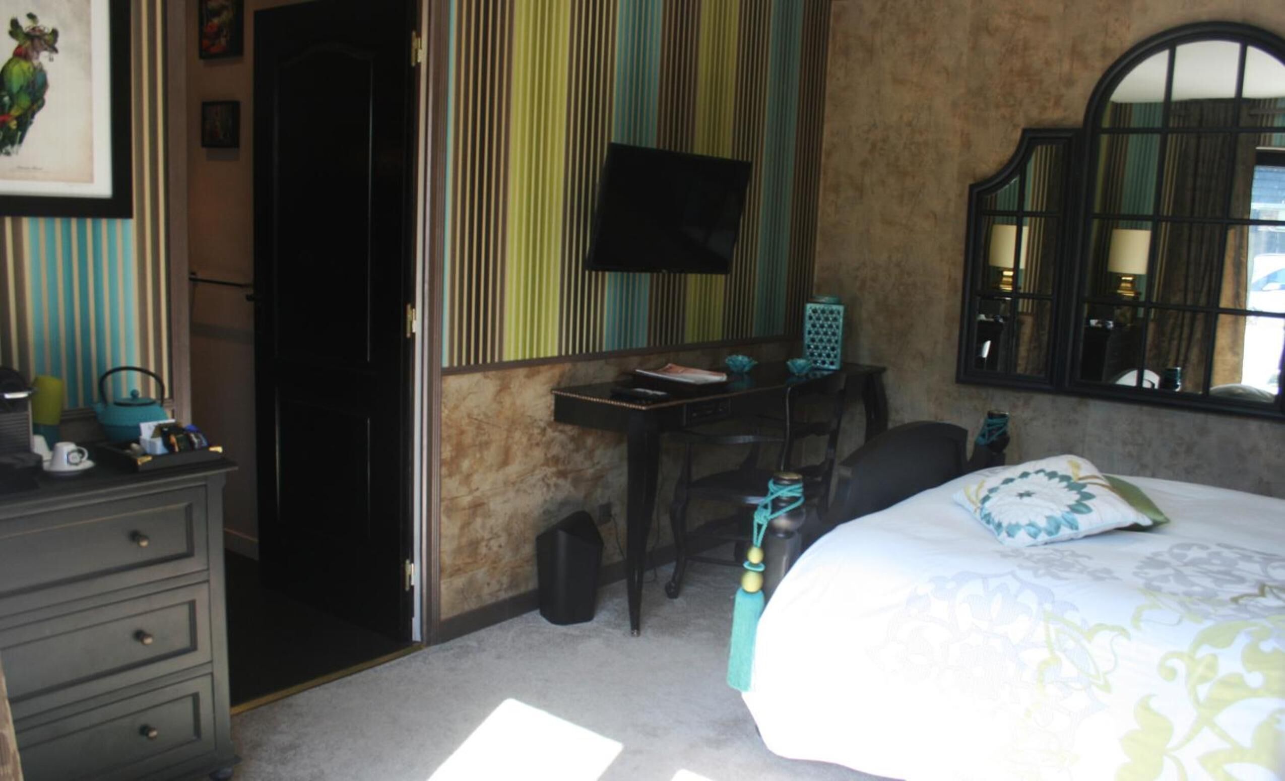 A bedroom with a bed, a desk, a chair, a dresser, a television, and a window.