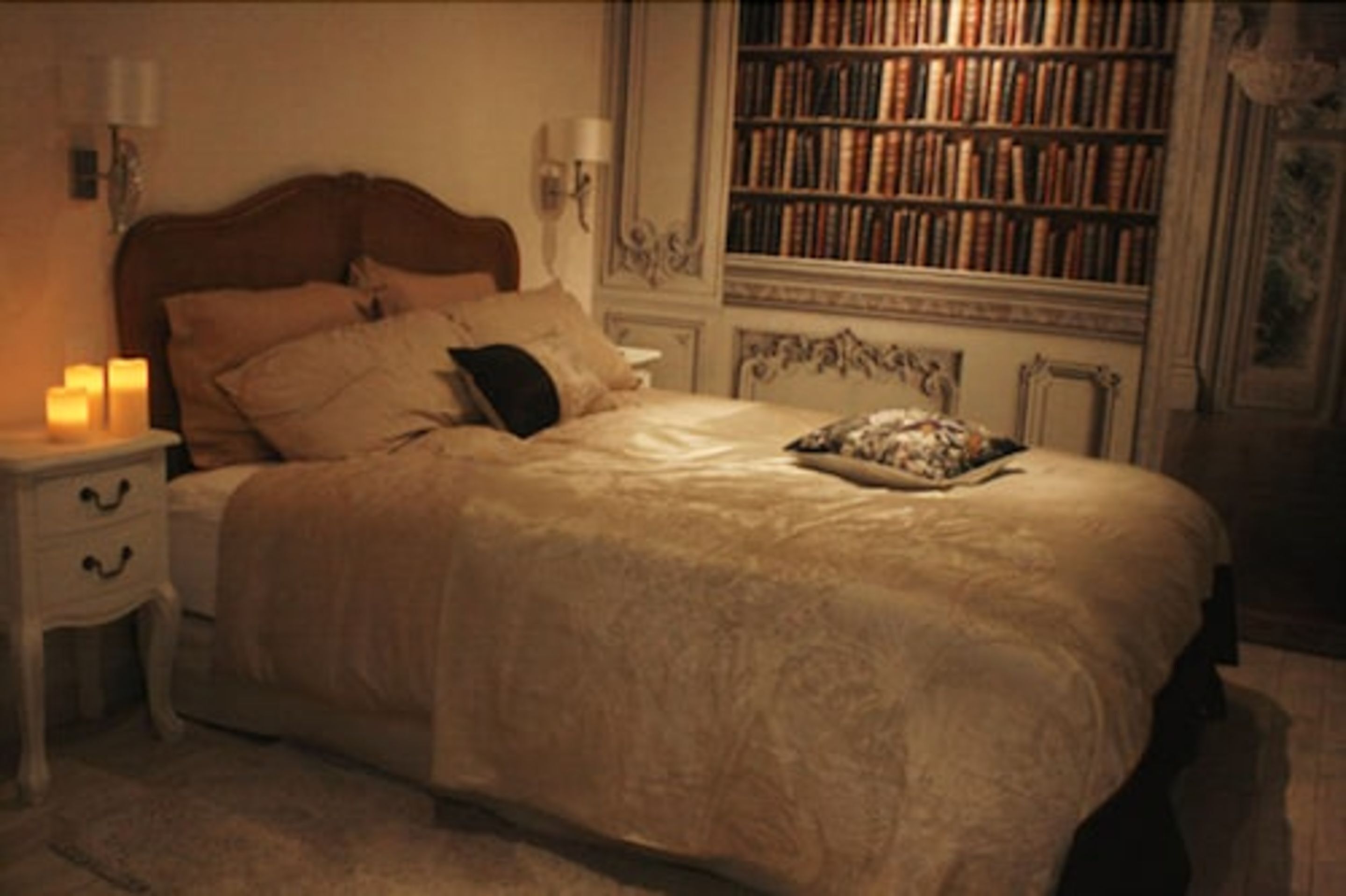 Une chambre avec un grand lit, une table de chevet avec une lampe et une bibliothèque en arrière-plan.