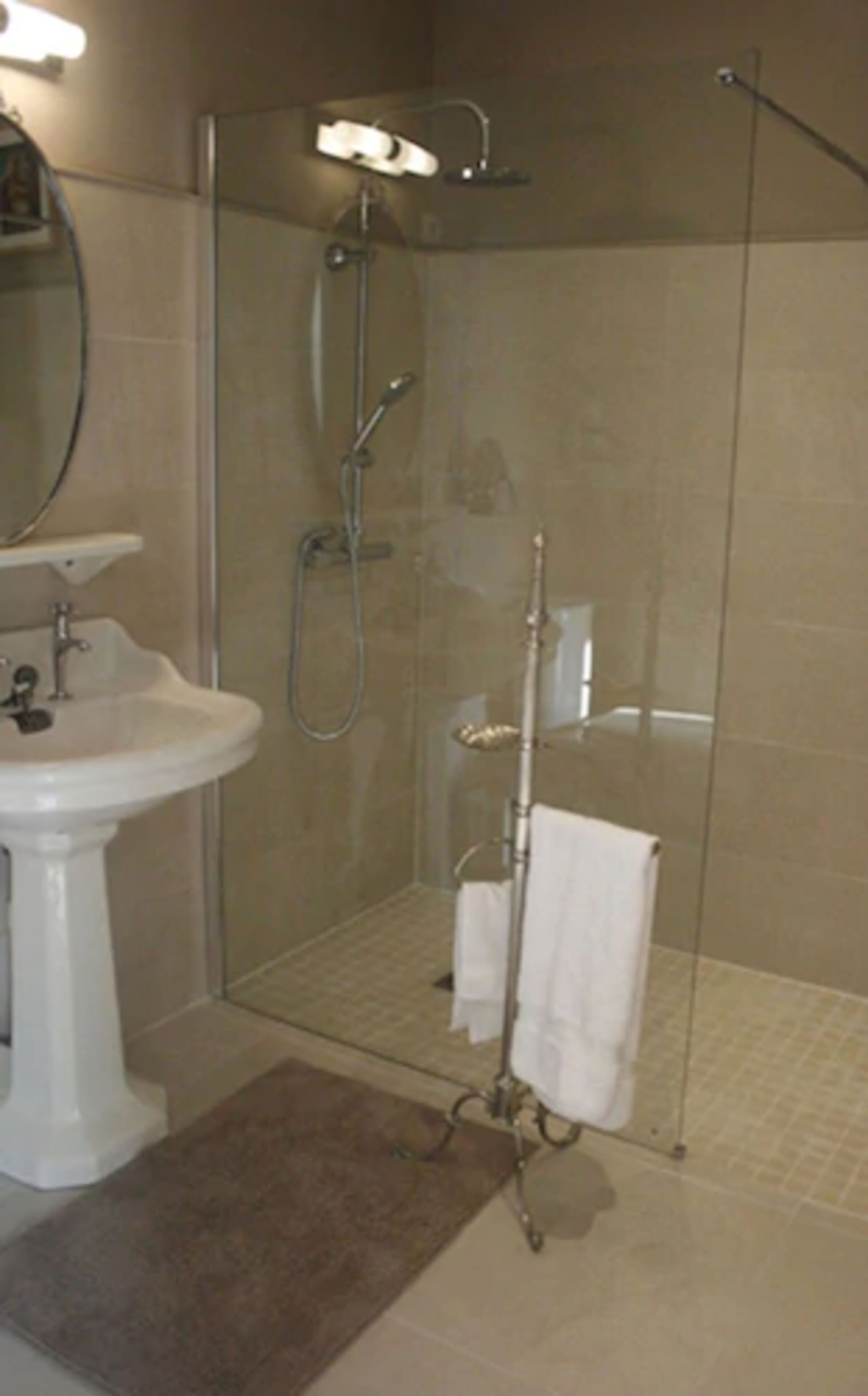 A modern bathroom with a glass-enclosed shower, a pedestal sink, and a mirror.
