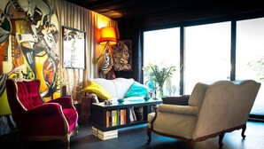 A living room with a red armchair, a beige armchair, a black bookshelf, and a large window with a view of greenery. - Kathome (Bondues)