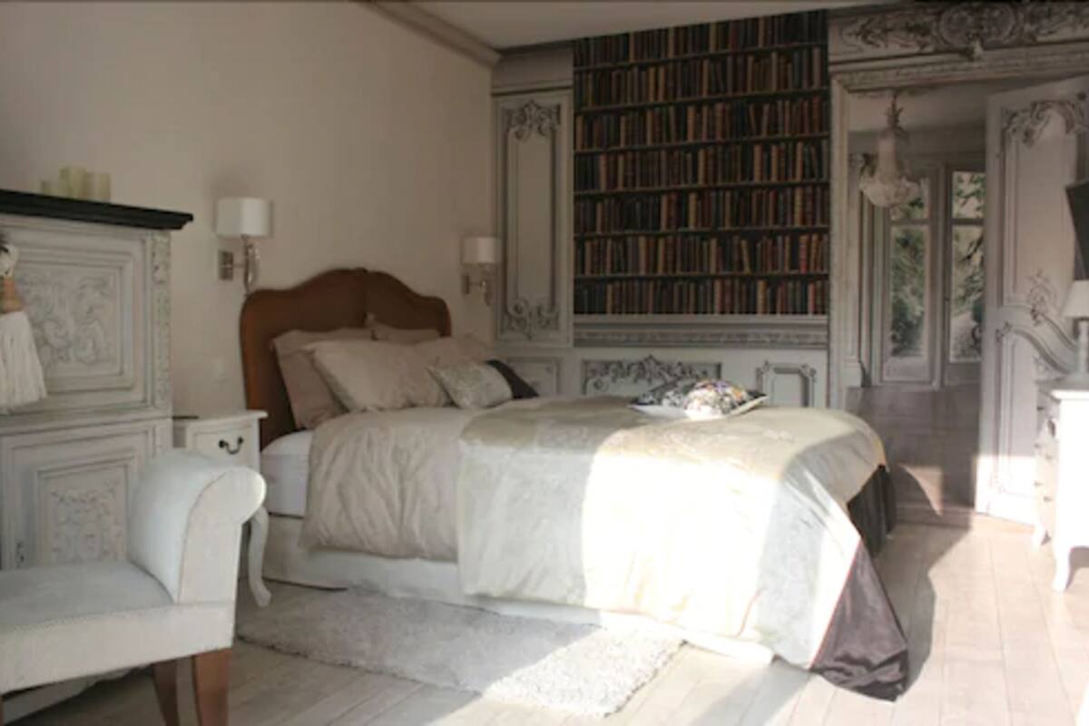 A bedroom with a large bed, a bookshelf, and a decorative fireplace.