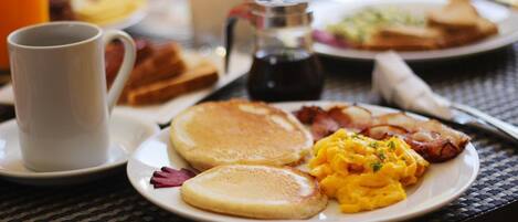 A breakfast plate with pancakes, scrambled eggs, bacon, toast, and a cup of coffee on a table.