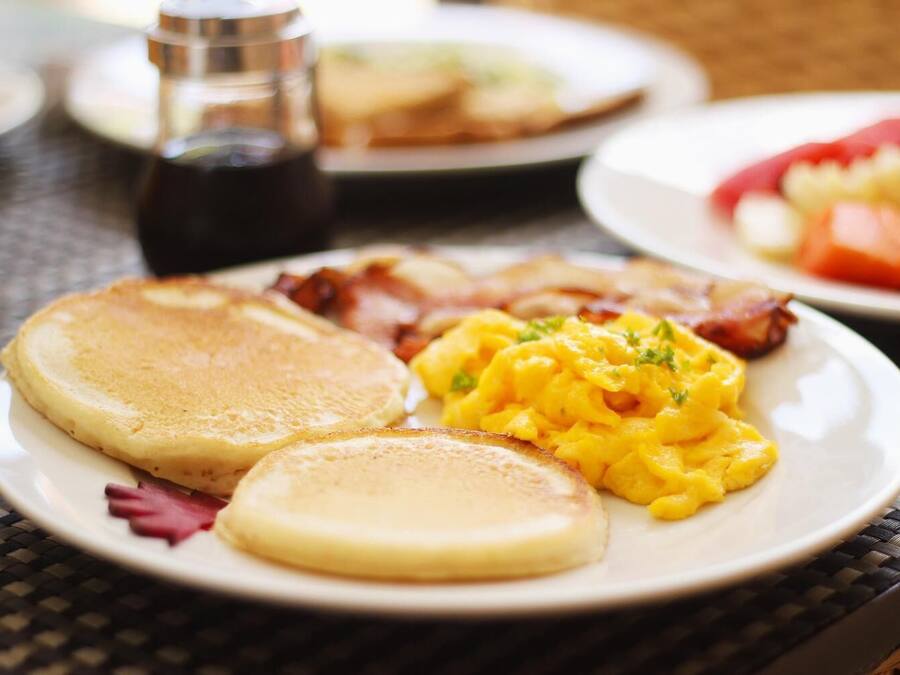 Un plato de desayuno con tortitas, huevos revueltos y tocino sobre una mesa.