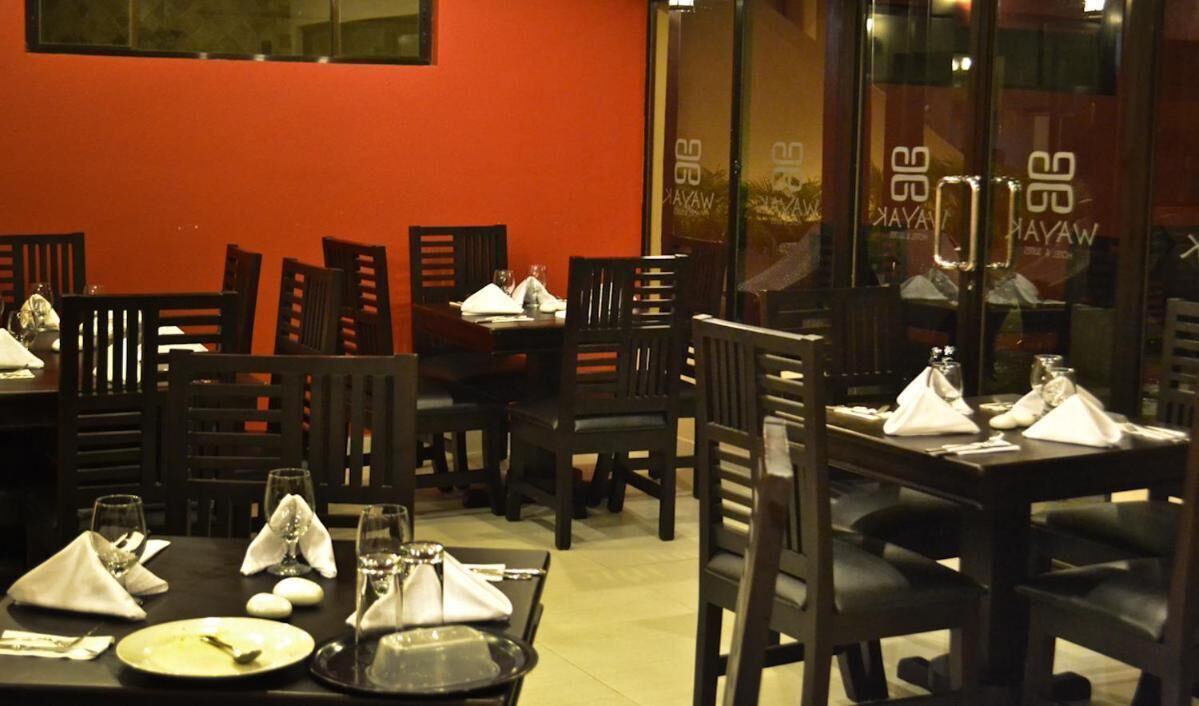 A restaurant with tables set for dining, chairs, and a red wall.