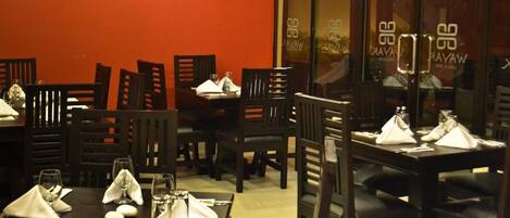 A restaurant with tables set for dining, chairs, and a red wall.