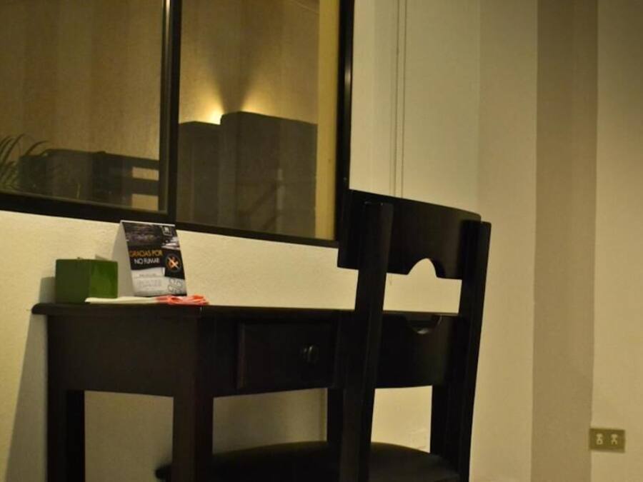 Une chaise en bois sombre, avec un miroir au-dessus, une petite boîte verte et un objet rouge posé sur l’assise de la chaise.