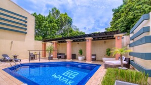 A swimming pool with the text "WAYAK" on the edge, surrounded by lounge chairs, a covered seating area, and potted plants. - Wayak Hotel & Suites (Managua)