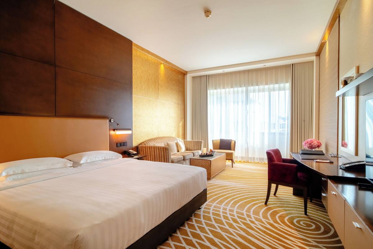 Ein Hotelzimmer mit einem großen Bett, einem Schreibtisch mit Computer, einem Sessel und einer Couch.