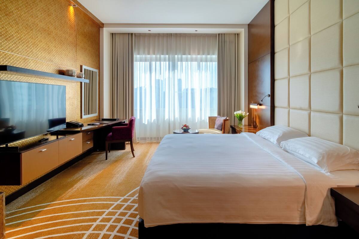 Ein Hotelzimmer mit einem großen Bett, einem Schreibtisch mit Stuhl, einem Fernseher und einem Fenster mit Vorhängen.