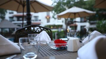 An outdoor dining table with a clear glass, a white napkin, a red flower, and a salt and pepper shaker.