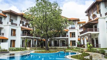 Un hôtel doté d’une piscine entourée d’une végétation luxuriante et d’un arbre au centre.