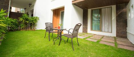 A courtyard with a table and chairs, surrounded by a well-maintained lawn and potted plants.