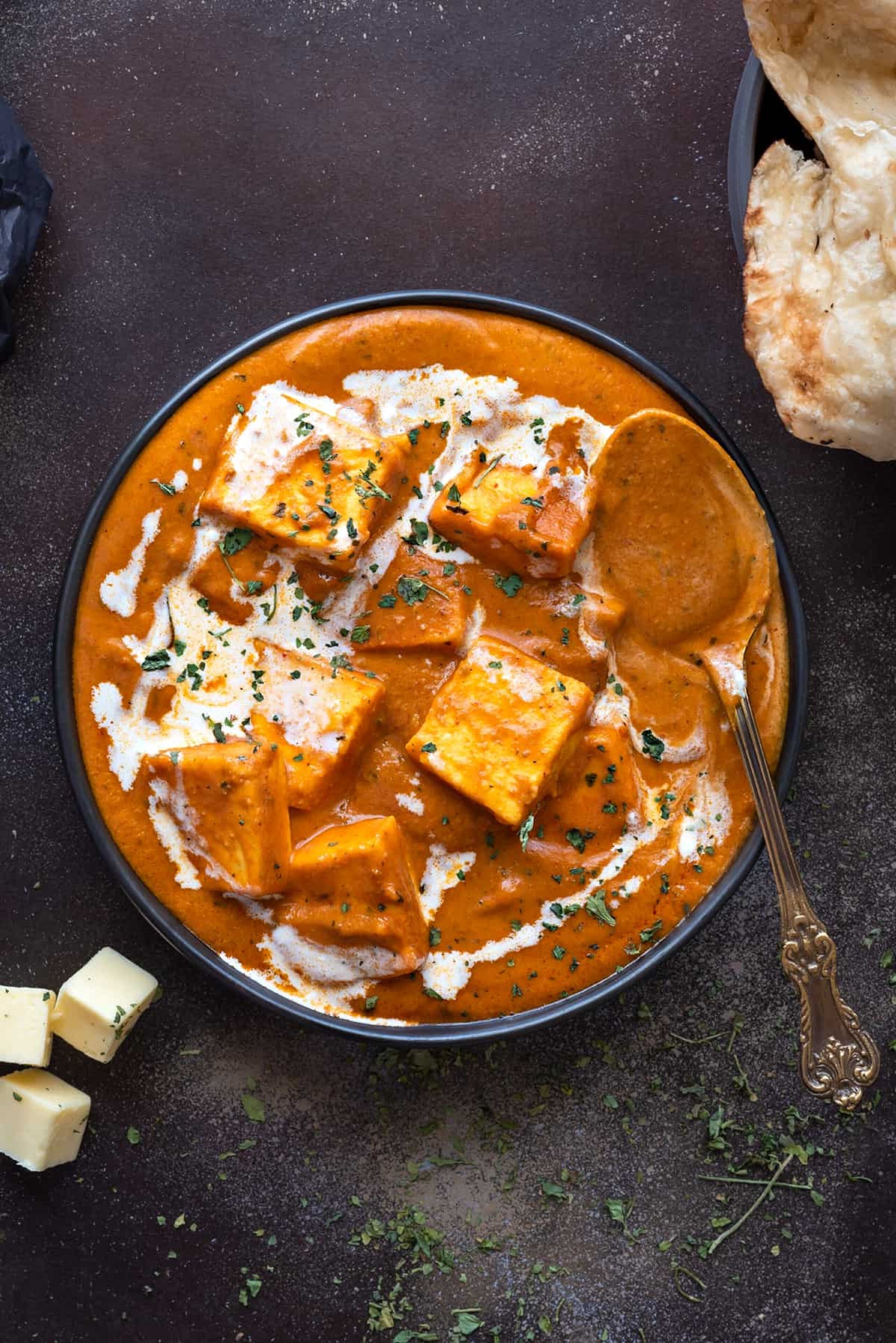 Una ciotola di curry di formaggio paneer, con cubetti di paneer e un cucchiaio.