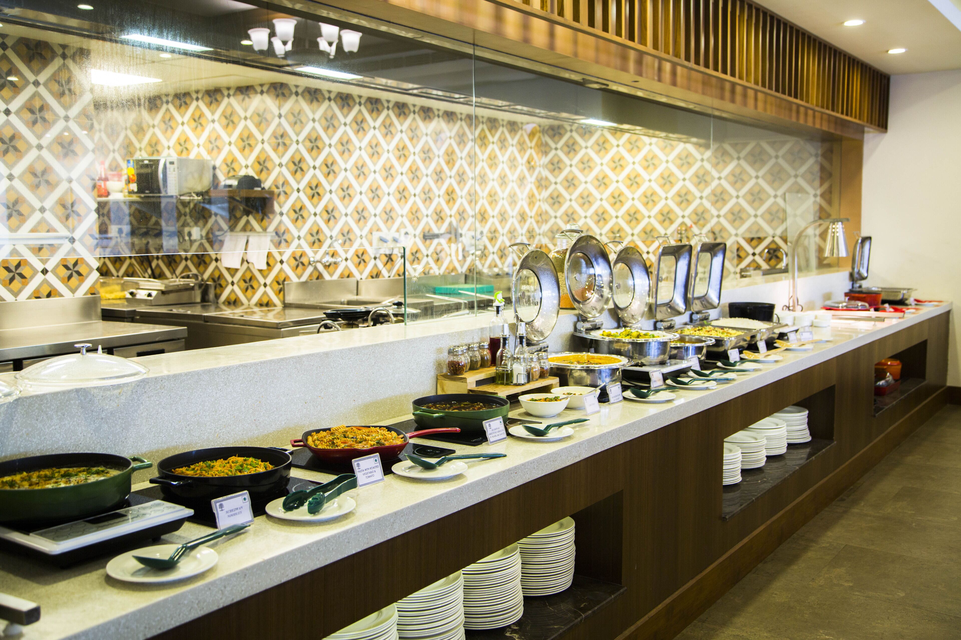 A buffet with various dishes and utensils, a tiled backsplash, and a counter with stacked plates.