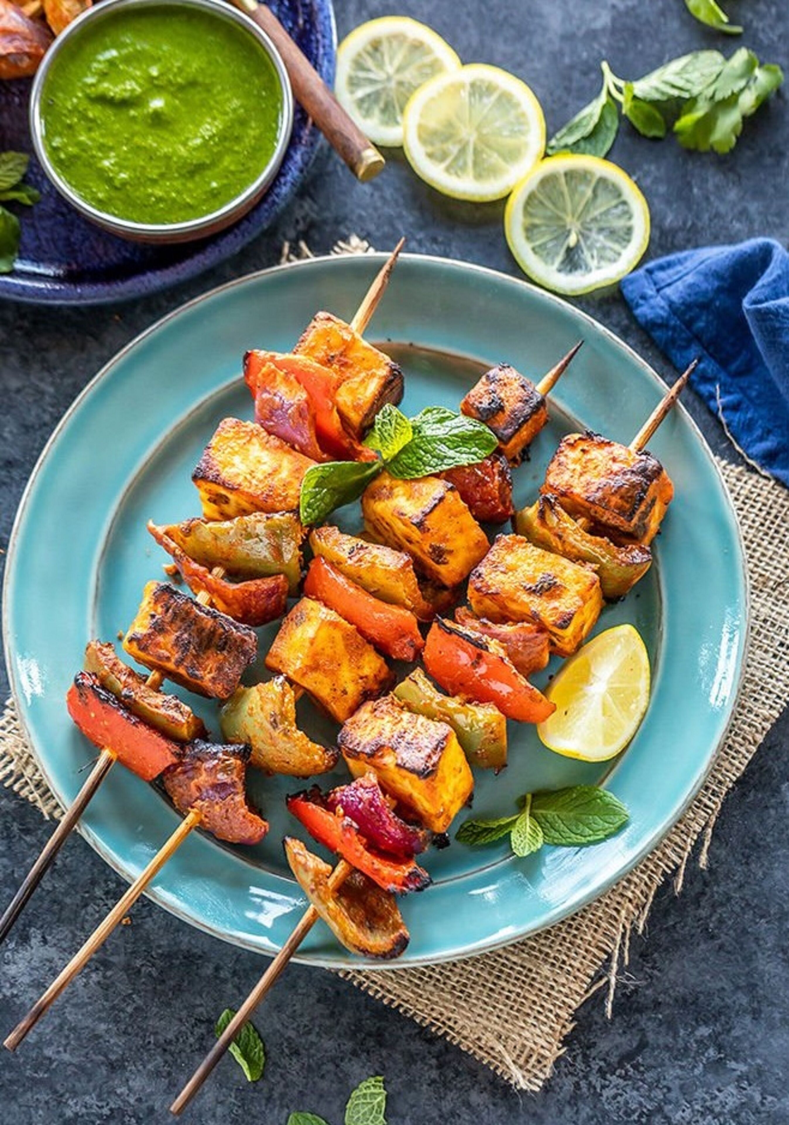 A plate of grilled vegetable and paneer skewers with a side of green chutney.