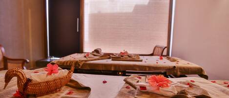 A room with two beds, each covered with a beige blanket and adorned with red flowers. A wicker boat with a pink flower rests on the floor near one bed.