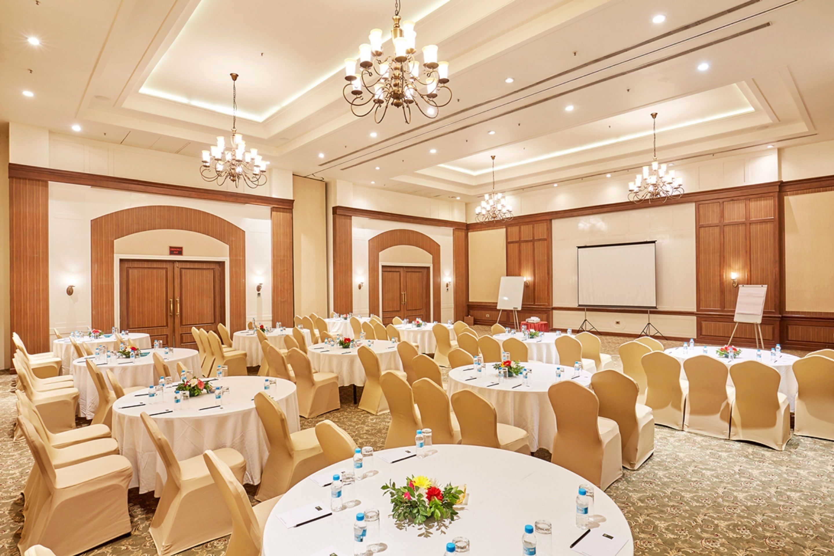 Une salle de conférence avec des tables rondes, des chaises de couleur beige et des lustres.