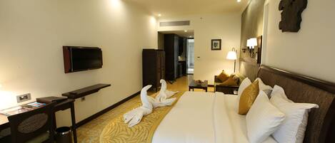 A hotel room with a bed, a desk, a television, a ceiling fan, and a hallway.