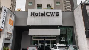 Un edificio alto de hotel con un letrero que dice "Hotel CWB" y "Andrade Hotels" en la fachada.
